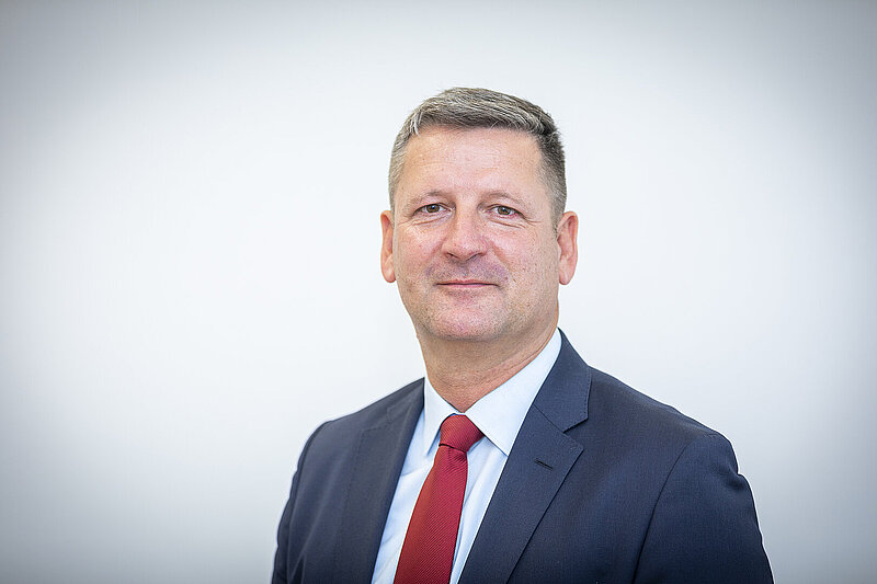 Porträt von Christian Bruch, Geschäftsführer der DGfM, im dunklen Anzug mit roter Krawatte.