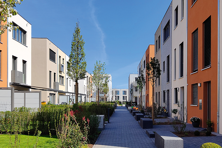 Moderne Wohnanlage mit begrüntem Innenweg, Reihenhäusern und mehrgeschossigen Wohngebäuden.