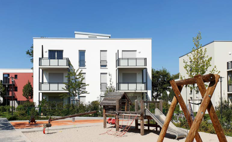 Mehrfamilienhaus mit Balkonen und Spielplatz im Vordergrund